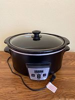 Full view of black Bella Kitchen slow cooker crock pot with glass lid and side handles on a wooden surface.