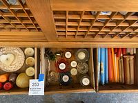 Overhead photo showing the assortment of candles, candleholders, and candle snuffers in a wooden drawer divided into three compartments.