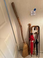 Overview photo of a carved wooden broomstick, umbrella, and walking sticks standing against a wall.