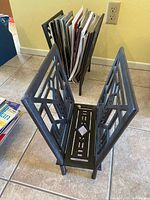 Two black cast iron magazine holders set up with magazines inside, showing the collapsible design and geometric pattern.