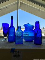 Full view of six cobalt blue glass vases and vessels displayed on a ledge with clear daylight background.