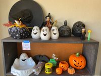 Wide photo of multiple Halloween decorations including ceramic pumpkins and ghosts, foam bat, caution tape, and small St. Patrick's Day sign.