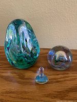 Two swirl style hand blown glass paperweights and a small glass spinning top on wooden surface.
