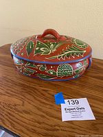Front side view of the oval hand painted terracotta casserole dish with butterfly and floral designs on lid and sides.