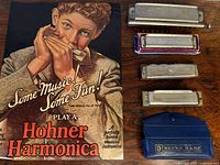Photo showing vintage advertisement poster with man playing harmonica and 5 vintage harmonicas in various cases and boxes.