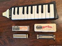Hohner Melodica and two Hohner Marine Band harmonicas with cases arranged on wooden surface.