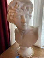 Front-facing photo showing the detailed face, curly hair, and winged cap of the marble bust.