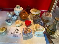 Image showing collection of assorted miniature trinket boxes arranged on white surface, including heart shapes and floral decorations, along with glass jars containing sand sculptures.