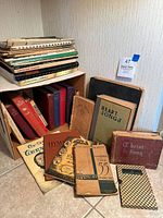 Photo showing a group of various music hymnals and song books stacked and arranged on the floor, including visible titles such as 'Heart Songs', 'Christ in Song', and others.
