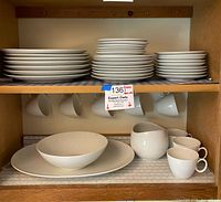 Multiple stacks of white plates in various sizes along with bowls, cups, and a large platter inside a wooden cabinet.