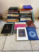 A stacked collection of approximately 38 religious books and booklets arranged on floor, including a variety of titles and formats such as hardcover, paperback, and spiral-bound booklets.