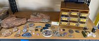 Photo showing the large rough stones on the left, polished agate slices spread out on the table, and a yellow drawer unit holding labeled drawers with various stone types including rose quartz, amethyst, lapis lazuli, tiger eye, amber, and moonstone.