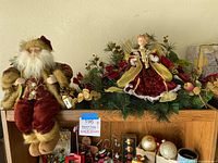 Full view of sitting Santa figurine next to angel tabletop display on shelf with other holiday items