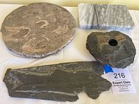 Four stone pieces on plain surface: polished round stone with fossils, slate fossil-like piece, slate flower holder, marble cheese board