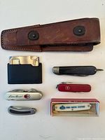 Photo showing five vintage pocket knives and a brown leather holster on white background.