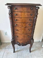 Front view showing the six drawers, round knobs, carved floral side columns, carved bottom apron, and cabriole legs.