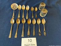 Full lot of spoons arranged on navy cloth with two glass condiment jars with sterling lids