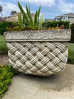 Front view of concrete planter showing basket weave pattern and succulents planted within.