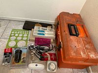 Wide shot of toolbox and tools including soldering irons, measuring tapes, stencils, and packaged hardware items