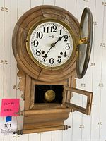 Front view of the wooden regulator wall clock with both glass doors open. Visible pendulum and clock face with Arabic numerals.