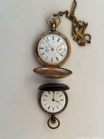 Photo showing both pocket watches, one with chain attached, both with white faces and Roman numerals.