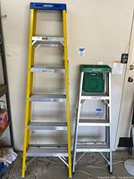 Full frontal view of both ladders side by side: 6-foot yellow fiberglass ladder and 4-foot aluminum ladder with green paint tray top