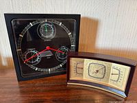 Photo showing two barometers side by side: a vintage wooden framed multi-scale barometer and a black square multi-dial contemporary barometer.