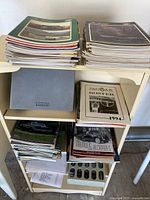 Shelf filled with stacks of vintage car magazines, pamphlets, catalogs, and documents including Lincoln Mercury and Jaguar materials.