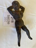 Full view of the vintage cast iron woman sculpture lying on a white cloth with a label beside it.