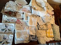 Overview of the full lot of vintage hand embroidered handkerchiefs in various folded states showing different embroidery motifs such as hearts, birds, and flowers.