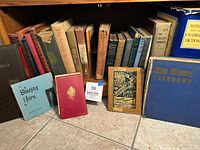 Shelf of vintage hardcover books with various titles showing wear and age on binding and covers, including Webster's dictionary and Air News Yearbook.