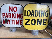 Both parking signs sitting side by side on a shelf, showing overall condition and mounting bases.