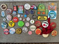 Photo showing about 40 vintage pins with political and expressive messages, including 'I Love Canada' pin with red ribbon and 'Editor 1990' rectangular pin patch.
