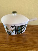 Full view of stoneware baking dish with lid showing abstract hen and floral design, handle and knob.