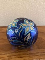Front view of spherical glass paperweight showing blue, yellow, and white floral patterns.