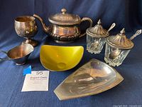 Front view of all items including teapot, goblet, sauce pot, condiment glasses, tray, and enamel dish on blue fabric background.