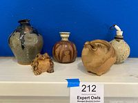 Five vintage stoneware and ceramic pieces including pots and figurines viewed against a blue background on a white surface.