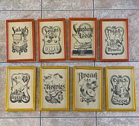 Overview of all 8 framed charcoal artworks displayed on floor tiles, showing different food themed designs and mixed frame colors.
