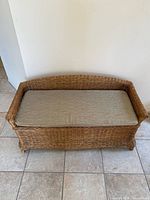 Front view of vintage wicker bench with beige seat cushion visible.