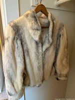 Front and side view showing the light-colored vintage fur jacket on a wooden hanger, highlighting texture and collar shape.