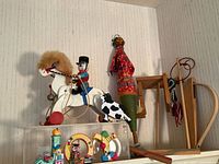 Wooden rocking horse with black spots and rider figurine, marionette puppet, wooden sled, and wooden push toys on shelf