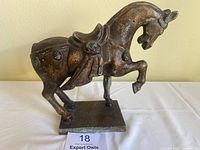 Side profile of vintage cast iron Chinese war horse statue with antique bronze finish, clearly showing raised front leg and ornamental saddle detail.