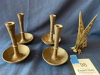 Four cast iron candlesticks and a brass butterfly candle holder displayed on a blue cloth background