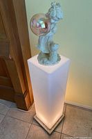 Full view of tall white lighted pedestal with figurine on top showing illuminated stand and detailed figurine.