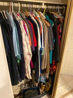 Full view of assorted women's clothing hanging on a rod including dresses, tops, jackets, scarves in various colors and styles