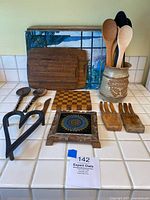 Overview of wooden kitchen utensils, cutting boards, forks, ceramic utensil holder, and pot trivet laid out on countertop.