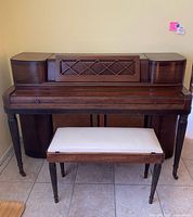 Front view of vintage Wurlitzer upright piano with matching bench, showing wood finish and design details.