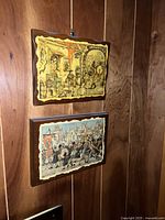 Two framed art prints by Anton Pieck hung on a wooden wall, showing detailed old-world scenes.