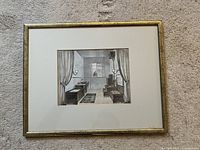Framed antique black and white bathroom scene art print shown from top-down angle on carpet background.