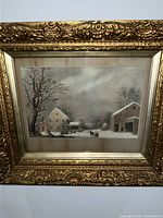 Close-up image of the framed winter landscape painting showing ornate gold frame details and the artwork depicting snow-covered buildings and a horse.